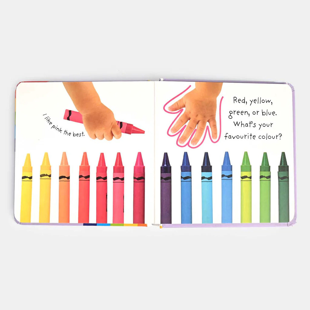 Children's book page with colorful crayons and hands holding a pink crayon.
