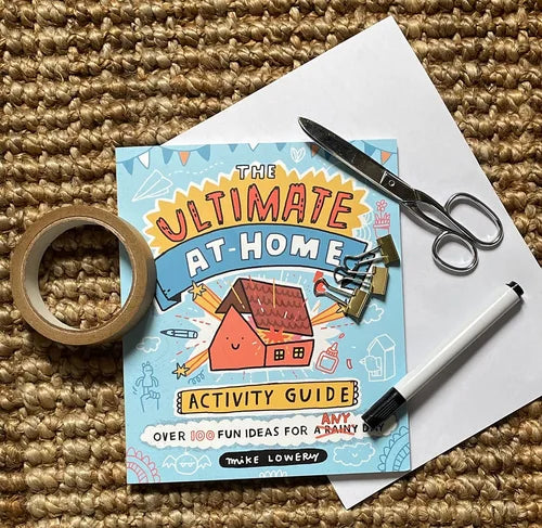 Activity guide titled 'The Ultimate At Home Activity Guide' with scissors, tape, and a marker on a textured surface.