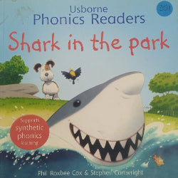 Cover of the book 'Usborne Phonics Readers Shark in the park' showing an illustration of a shark with open mouth, a small bird, a bee, and a child reading a book.